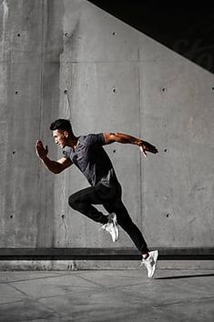 a young man is jumping in the air with his skateboard near a concrete wall