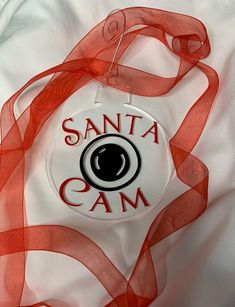 the santa cam badge is attached to a white shirt with red ribbon around it's neck