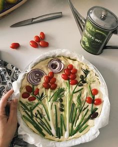 a person is making a pizza with vegetables and herbs on it, along with other food items