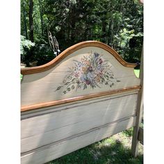 an old bed frame with flowers painted on the top and bottom part, in front of some trees