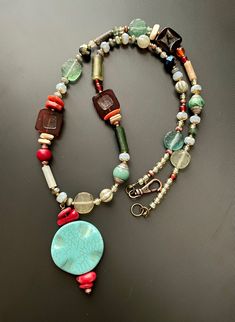 "Old and new come together in this stunning and eclectic holiday pendant necklace. Ancient Roman Glass beads nicely scattered with an eclectic mix of sparkle and color, including three modern red glass tile beads, all anchored with a light blue circular pendant.  This piece measures approx 25.5\" with two inch extension chain, finished with a decorative antique copper lobster claw clasp."