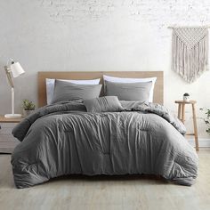 a bed with grey sheets and pillows in a white room