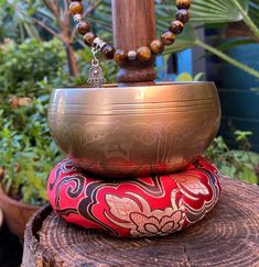 a metal bowl sitting on top of a tree stump with beads hanging from it's sides