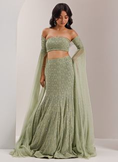 Step into elegance with the Mint Green Mermaid Jaal Lehenga, a striking fusion of sophistication and glamour. Crafted from luxurious organza and shimmer chiffon,, this stunning mint green lehenga showcases intricate crystal and cut dana embroidery in a captivating snowflake jaal design. The soft, flowing lehenga is enhanced by the mermaid cut, which flatters the figure while maintaining an ethereal grace. Paired with an off-shoulder blouse featuring dramatic, floor-length sleeve. Standout lehenga choice for Mehndi, Sangeet, or as wedding guest attire. Composition : Lehenga, Blouse - Organza, Shimmer Chiffon, and Chantoon Care: Dry Clean Only and Vacuum Storage This product can be customized for sleeves, blouse length and neckline Delivery : 6-8 weeks as the product is hand crafted. Check S Mermaid Cut Lehenga, Udaipur Outfits, Unique Lehenga Designs, Mermaid Lehenga, Indian Engagement Outfit, Mint Green Lehenga, Off Shoulder Lehenga, Blouse Organza, Mint Green Blouse