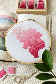 the cross stitch pattern is being displayed in front of an open book with scissors and thread spools