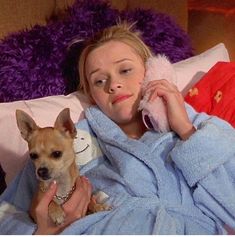 a woman laying in bed with a dog on her lap and talking on the phone