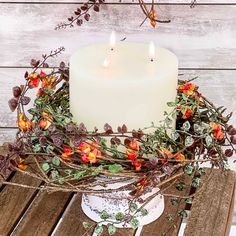 a white candle sitting on top of a wooden table next to some branches and flowers