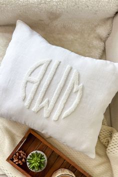 a white pillow with the word monogrammed on it next to a bowl of succulents