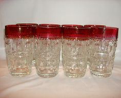 four red glass tumblers lined up on a white tableclothed surface, with one in the middle