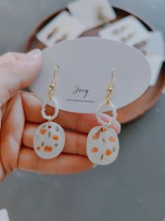 a pair of white and orange earrings with flowers on them, in front of a mirror