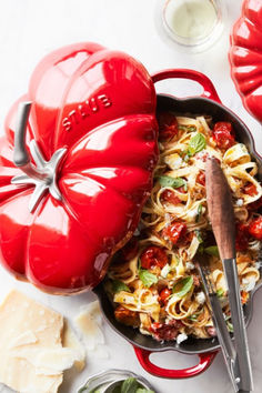 a skillet filled with pasta and tomatoes next to other ingredients on a white surface