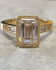 an emerald cut diamond ring with two baguets on the band and side stones