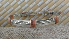 Bangle of silver wire banded with copper. Silver clasp. 7" circumference. Nickel Free Copper Bracelet In Silver, Hand Wrapped Silver Metal Bracelets, Hand Wrapped Silver Cuff Bracelet, Hand Wrapped Silver Metal Bracelet, Adjustable Silver Copper Jewelry, Hand Wrapped Silver Round Cuff Bracelet, Silver Copper Bracelet For Gift, Silver Metal Hoop Bracelets, Nickel Free Copper Bangle