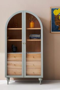 a book shelf with books and vases on it in front of a pink wall