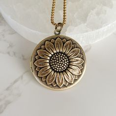 "Now offering custom engraving.  Visit shop for details. Capture the essence of nature with this stunning antique gold sunflower locket. The intricate details of the sunflower design make this locket a true masterpiece that will be cherished for years to come. The locket is 32mm in diameter and made of high-quality antiqued brass that opens to reveal a secret compartment for keeping your most treasured memories close to your heart. The antiqued brass link chain with a lobster clasp adds a touch of vintage elegance to this timeless piece of jewelry. You can choose from 18\", 20\" or 24\" length to suit your style. The smooth brass backside of the locket gives it a sleek and polished look. The locket can hold two 25mm inserts, which is perfect for keeping pictures, messages, or any other sma Gold Jewelry With Flower Charm Keepsake, Gold Necklace With Antique Finish For Keepsake, Vintage Gold Necklace For Mom, Vintage Adjustable Sunflower Design Jewelry, Bohemian Gold Keepsake Jewelry, Wedding Jewelry With Sunflower Design, Vintage Medallion Jewelry With Flower Charm, Anniversary Gold Jewelry With Sunflower Design, Antique Finish Round Pendant Jewelry For Gift