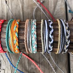 several different colored bracelets are arranged on a wooden stick and tied together with twine