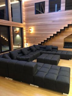 a living room filled with black couches next to a stair case and wooden floors