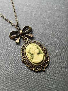 Victorian Lady Cameo Necklace, Charming Sweet Vintage Inspired Necklace, Victorian Gothic Jewelry, Vintage Wedding Gift, Bridesmaid Gift, Vintage Inspired Jewelry  This is a sweet Victorian cameo lady necklace dangling from a cute brass bow of the valley locket necklace and a dainty necklace. This adorable Victorian era style necklace comes in four colors, pick the color that best suits your style, taste, or vintage wedding theme.   This Victorian style necklace is very versatile, it can be a bridesmaid gift, but it can also be an everyday necklace. ❤ Available Colors: Sage Green Cameo Lady Purple/ Lavender Cameo Lady Rose Pink Cameo Lady Olive Green Cameo Lady ❤ Pendant size:  1" Long by 3/4" wide, 1 3/4 inches including the bow Necklace Length: 16 inches- 24 inches  ❤ All items are handm Lady Cameo Necklace, Victorian Gothic Jewelry, Necklace Drawing, Victorian Accessories, Vintage Wedding Gifts, Vintage Wedding Theme, Bow Necklace, Victorian Lady, Vintage Inspired Jewelry