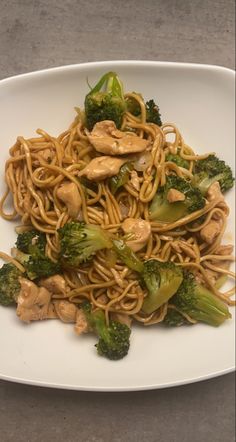 a white plate topped with noodles and broccoli covered in peanut sauce on top of a table