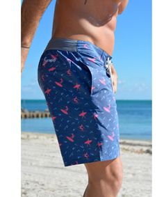 a man with no shirt on standing on the beach wearing blue and pink swim trunks