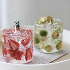 two glasses filled with water and strawberries on top of a white tray next to each other