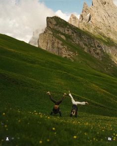 two people are standing in the grass with their arms up and legs spread out as if they are doing yoga