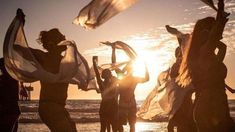 some people are dancing on the beach at sunset