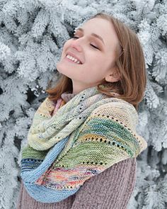 a woman standing in front of snow covered trees wearing a multicolored shawl