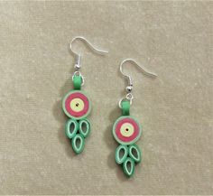 two pairs of green and red earrings on a beige surface with white thread, beads and metal hooks