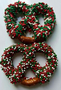 three donuts decorated with sprinkles and colored frosting on white surface