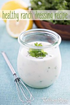 a glass jar filled with ranch dressing next to a whisk and lemon wedges