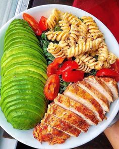 a white plate topped with meat, pasta and veggies next to a sliced cucumber