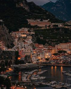 boats are docked in the harbor at night near some buildings and mountains with lights on them