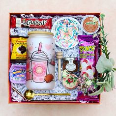 an assortment of snacks and candy in a gift box on a pink surface with a succulent