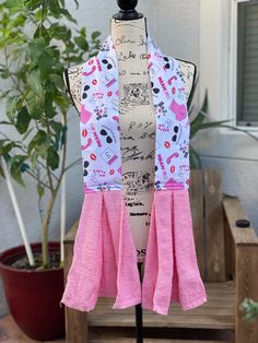 a mannequin with pink and white scarfs on it's neck, sitting in front of a potted plant