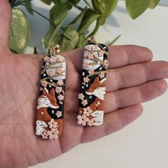 a pair of earrings with flowers and birds on them are being held by a person's hand