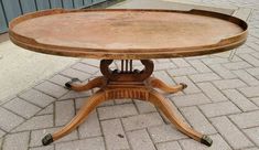 an old wooden table sitting on top of a brick floor next to a sidewalk with a bench in the background