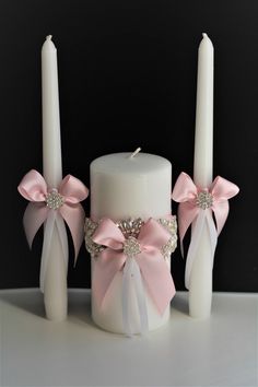 two white candles with pink bows on them