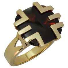 This gorgeous Cartier cocktail ring is crafted in 18k yellow gold and features a cabochon garnet set in a geometric crown. The 14.7mm x 14.9mm buff-top cushion-shaped garnet has dark red color with brownish tones, a fairly good transparency with some inclusion visible upon close inspection, and surface wear in form of fine scratches visible upon close inspection. Made in France circa 1970s. Measurements: 0.66" (17mm) width, 0.66" (17mm) length. The ring size is 6.25 - EU 53. Resizable. Sizing fees will be provided upon request. Modern Gold Signet Ring With Cabochon, Modern Yellow Gold Signet Ring With Cabochon, Modern Gemstone Dome Ring For Formal Occasions, Modern Dome Ring With Gemstone For Formal Occasions, Modernist Formal Cabochon Rings, Oval Cartier Rings For Formal Occasions, Luxury Cabochon Signet Ring For Formal Occasions, Luxury 14k Gold Ruby Cabochon Ring, Luxury Yellow Gold Rings With Garnet