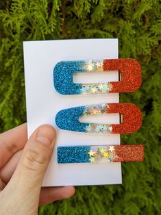 someone is holding up two magnets that have glitter on them and are red, white, and blue