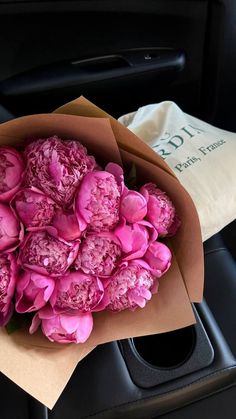 a bunch of pink flowers in a brown paper bag sitting on the back seat of a car