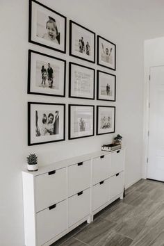 a white wall with black and white pictures on the wall above it is filled with drawers