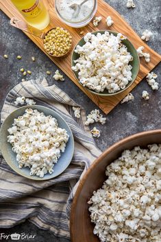 two bowls filled with popcorn sitting on top of a wooden cutting board next to other food