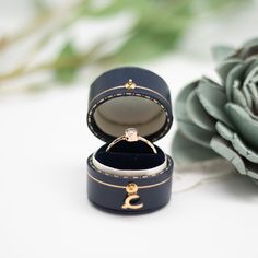 an open ring box sitting next to a flower