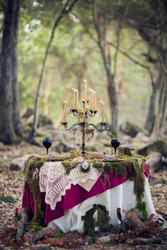 an image of a table with candles in the middle and moss growing on it, surrounded by trees