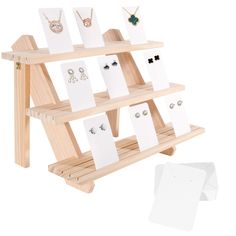 a wooden display case with earrings and necklaces on it, next to white paper