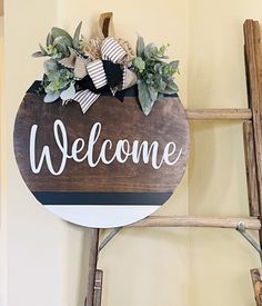 a wooden sign that says welcome hanging on a wall next to a ladder with plants