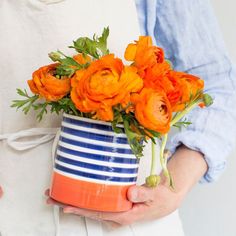 a person holding a blue and white striped vase with orange flowers in it's hands