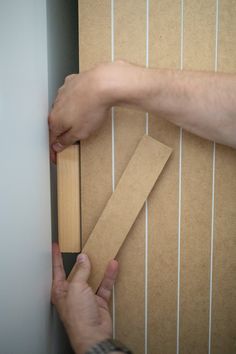 a person holding a piece of wood in front of a wall with strips of cardboard taped to it