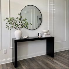 a black and white console table with a mirror on the wall above it, along with a potted plant